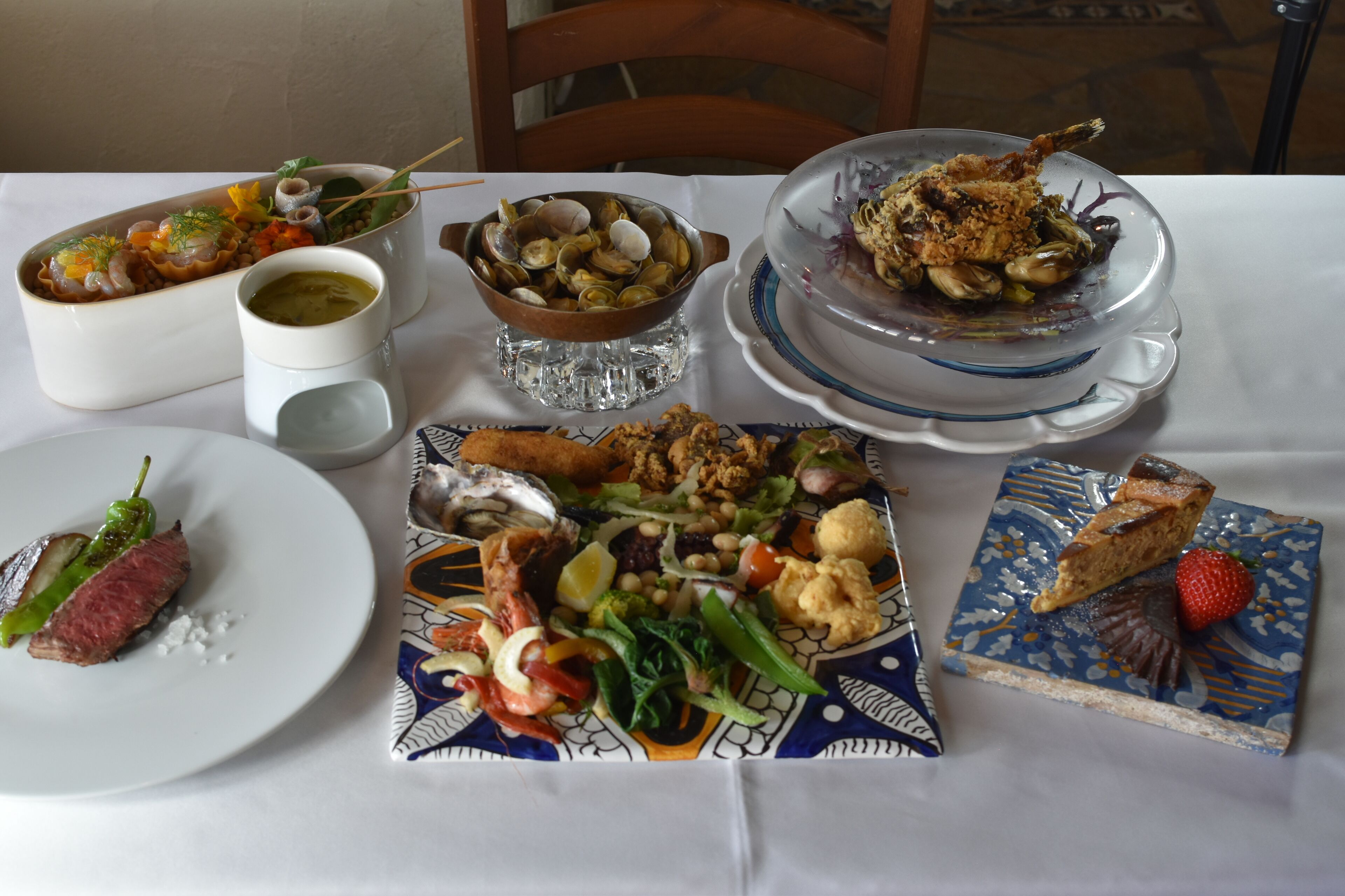 Una mesa servida con diversos platos, incluyendo mariscos, un bistec y un postre.