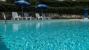 A clear swimming pool with blue water, surrounded by white lounge chairs and blue umbrellas. - Casa Gioele D: A welcoming apartment situated in a quiet location, a few minutes from the town center, with Free WI-FI. (Umbertide)