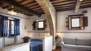 A rustic room with exposed wooden beams, a bed with a blue bedspread, a grey sofa, and a small window with wooden shutters. - Casa Gioele D: A welcoming apartment situated in a quiet location, a few minutes from the town center, with Free WI-FI. (Umbertide)