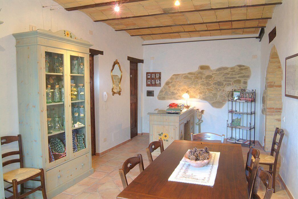Uma sala de jantar com uma mesa de madeira, cadeiras, um armário com portas de vidro e uma parede de pedra.