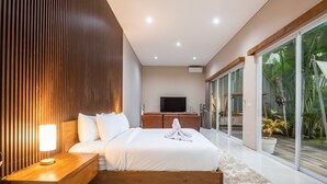 A modern bedroom with a large bed, wooden panel wall, bedside table with lamp, and a TV. - Luxury PrivatePoolVilla Lumiere Dewi Sri (Legian)