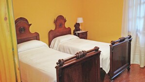 Ein Zimmer mit zwei Holzbett, einem Nachttisch mit Lampe und einem Fenster mit Vorhängen.
