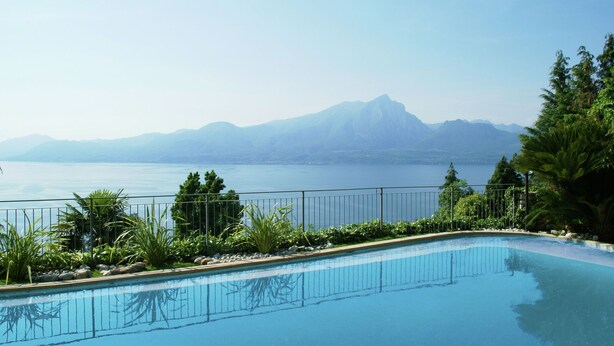 Ein Schwimmbecken mit Blick auf ein Gebirge und ein Gewässer.