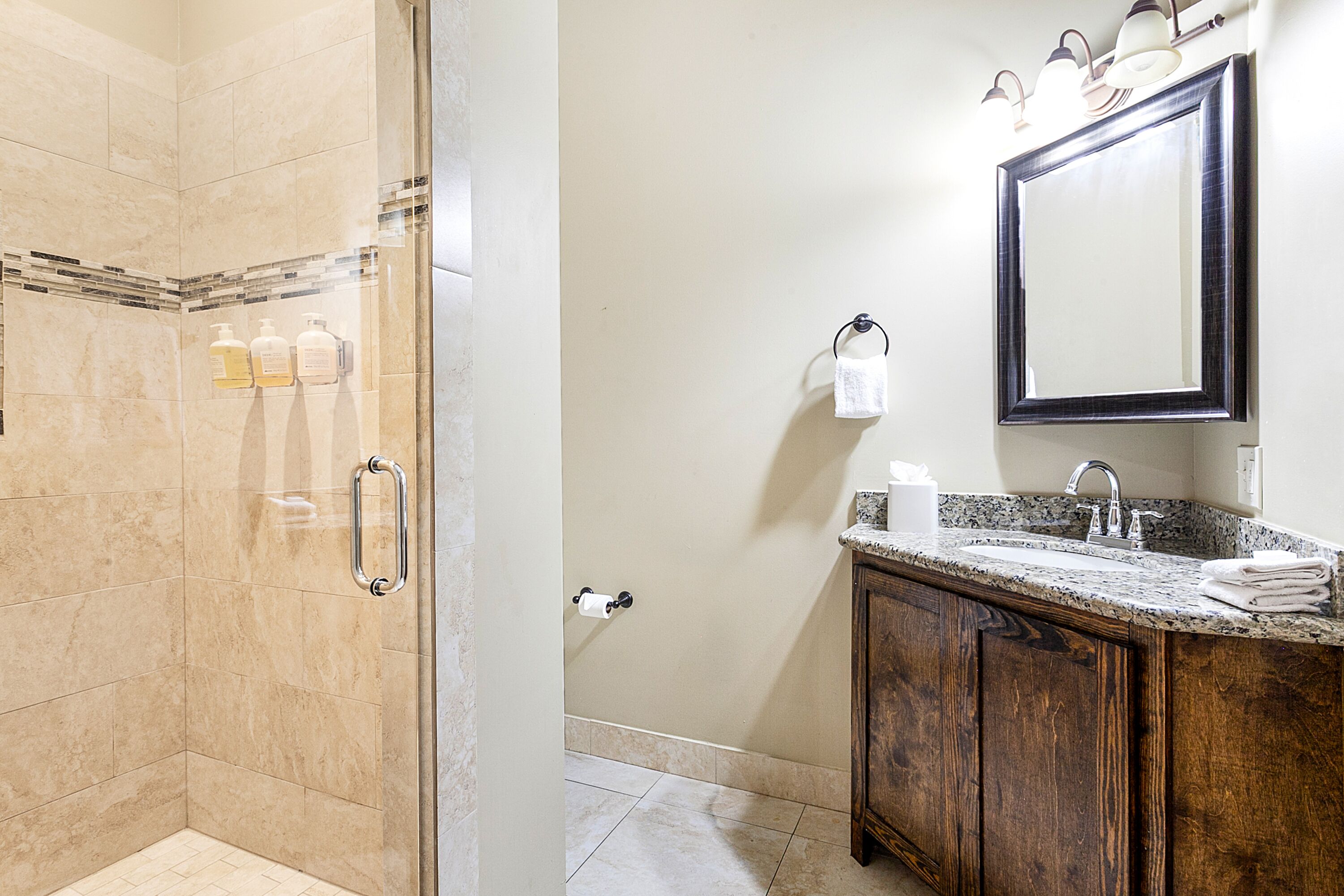 Une salle de bain dotée d’une douche à parois de verre, d’un meuble-lavabo en bois et d’un miroir au-dessus du plan de travail.