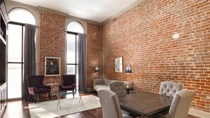 A room with a brick wall, a dining table with four chairs, two armchairs, and a glass coffee table. - Chuck's place (New Orleans)