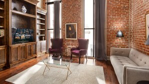 A living room with a brick wall, a sofa, two armchairs, a glass coffee table, a TV, and a bookshelf. - Chuck's place (New Orleans)