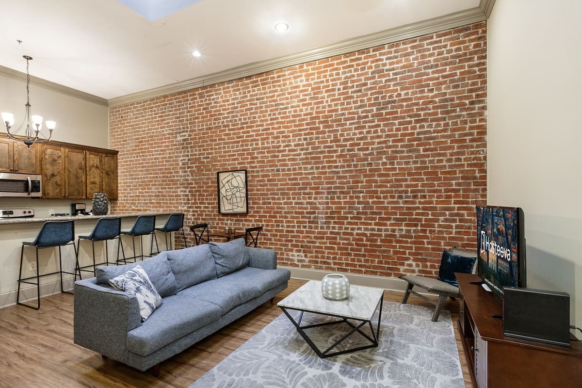 A modern living room with a brick wall, a grey sofa, a coffee table, and a TV.