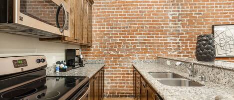 A kitchen with a brick wall, wooden cabinets, a stainless steel sink, and a granite countertop.