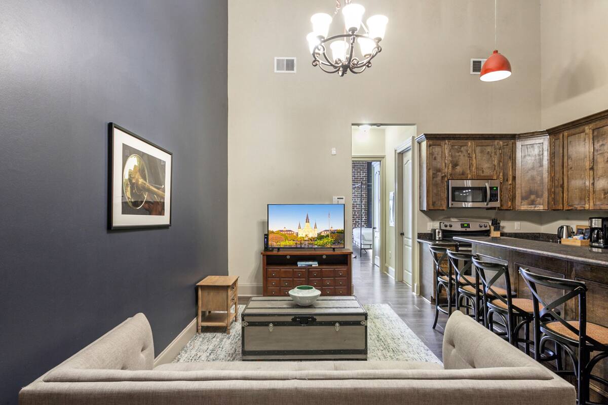 A modern kitchen with a microwave, stove, and bar area. There is a television on a stand in the living room, and a framed picture on the wall.