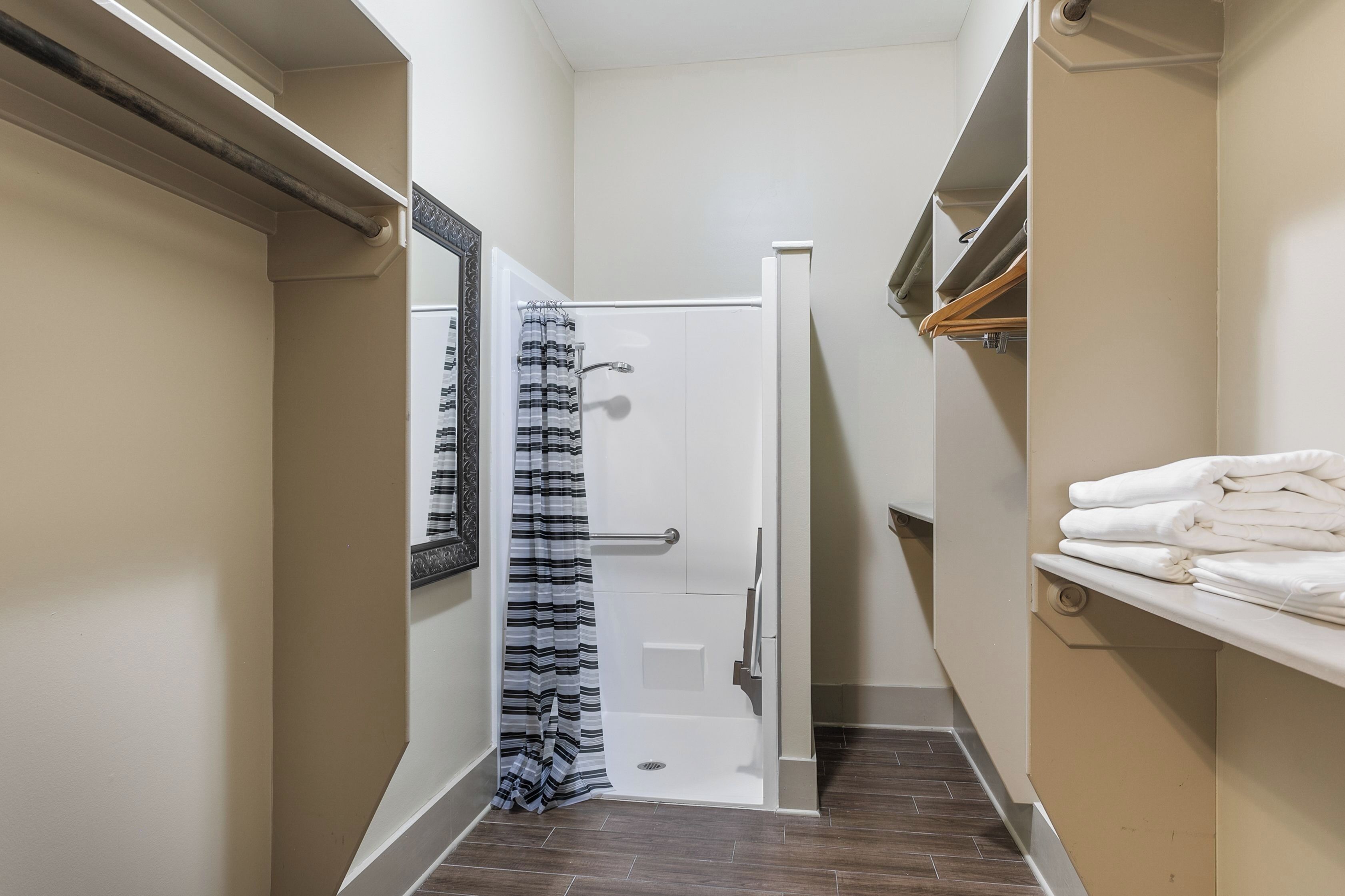 A narrow hallway with a shower, a towel rack, and a mirror.