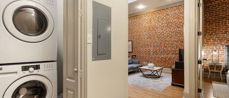 A laundry room with a front-loading washer and dryer, a brick-patterned living room with a sofa and coffee table, and a skylight above the laundry area.