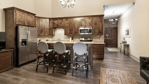 A modern kitchen with wooden cabinets, stainless steel appliances, and a bar area with patterned stools. - Chuck's place (New Orleans)