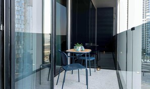 Un balcon moderne avec une porte vitrée, une petite table avec des chaises et une plante en pot.