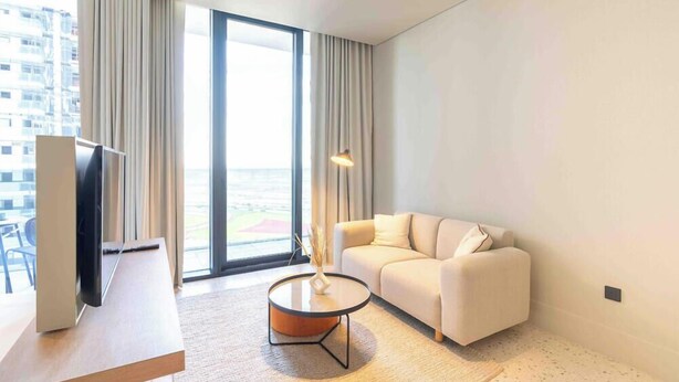 A modern hotel room with a sofa, a coffee table, a TV, and a large window offering a view of the city. - Prime Location, Pristine Studio in Business Bay (Dubai)