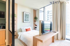Ein modernes Hotelzimmer mit Bett, Schreibtisch mit Fernseher, Fenster mit Vorhängen und Blick auf die Stadt.