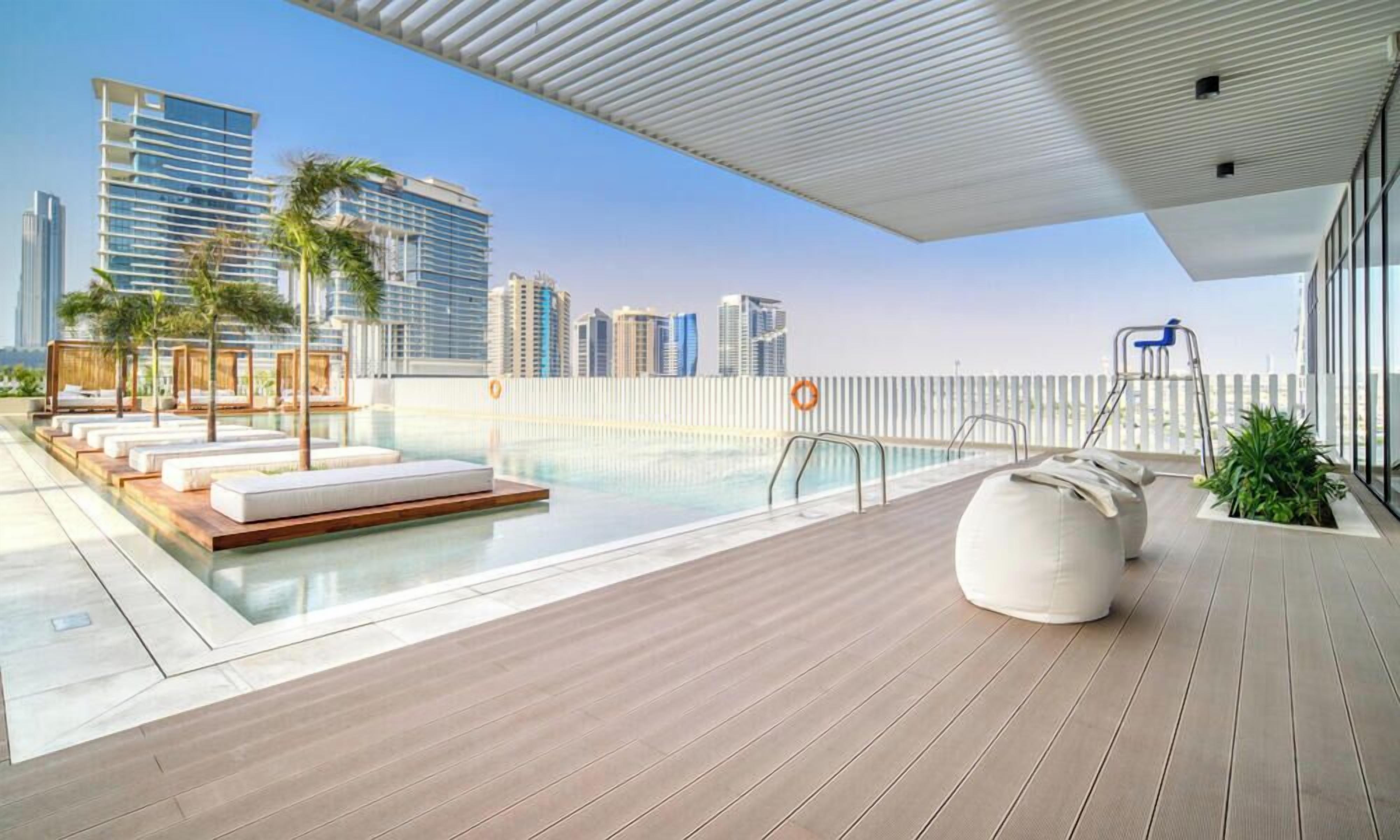 Et moderne tagområde med swimmingpool, liggestole, træterrasse og udsigt til byens skyline.