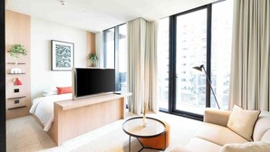 Ein modernes Hotelzimmer mit einem Bett, einem Fernseher, einem Sofa, einem Couchtisch und großen Fenstern mit Vorhängen.