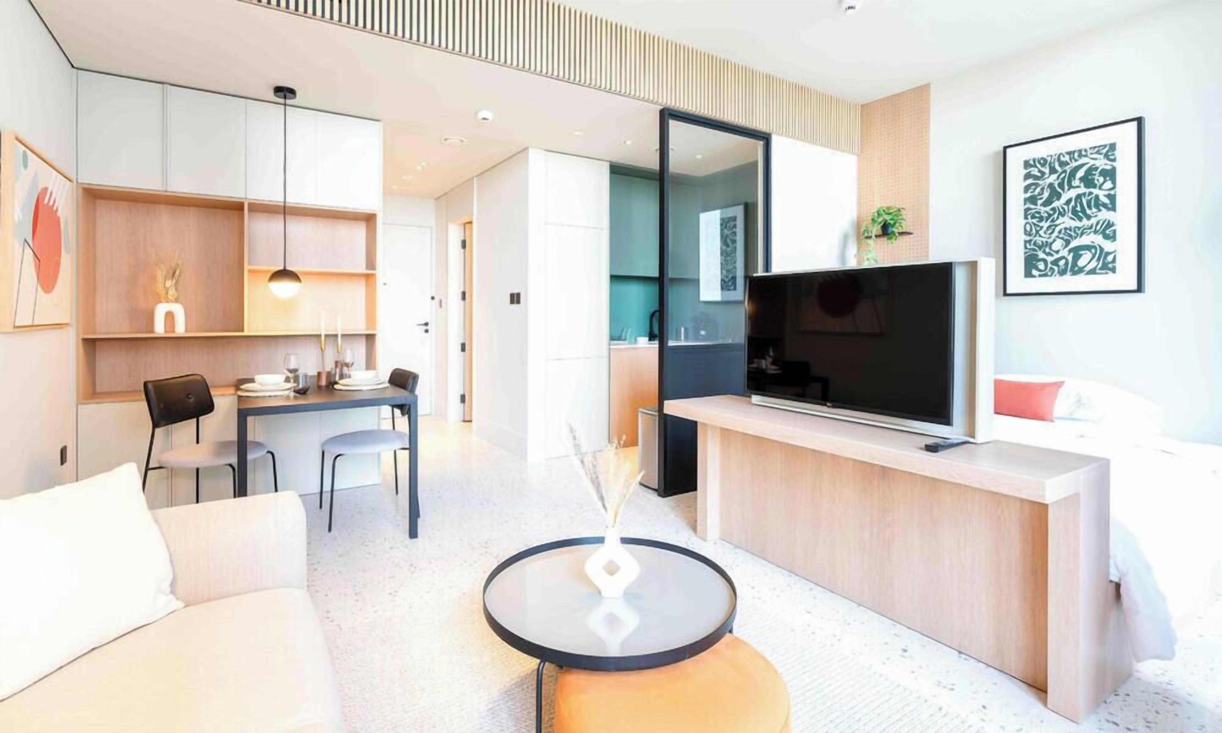 Una sala de estar moderna con un sofá, una mesa redonda de centro, un televisor y un comedor con sillas y una mesa.