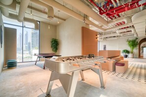 Un espace intérieur moderne doté d’un baby-foot, de grandes fenêtres et offrant une vue sur le paysage urbain.
