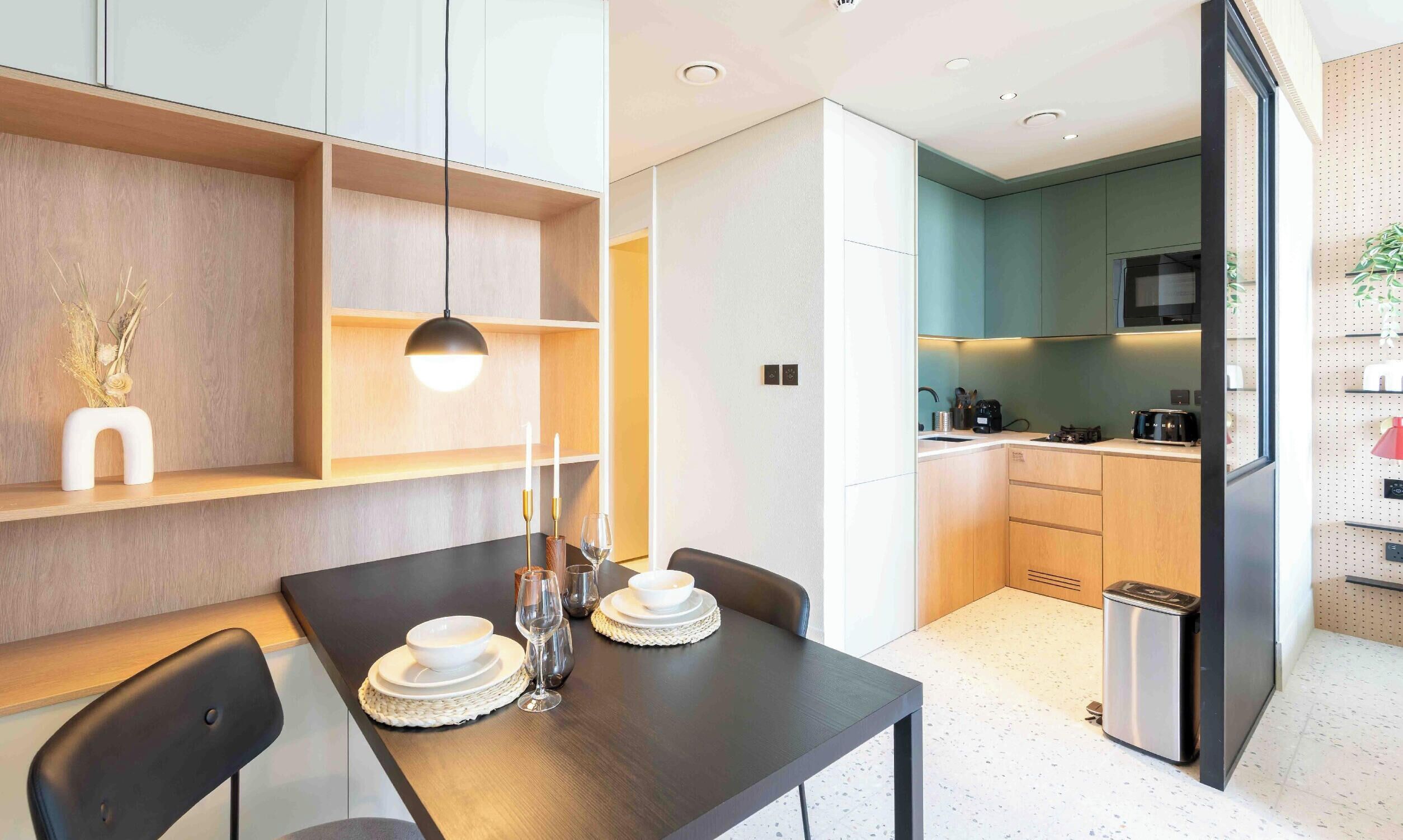 A modern kitchen with a dining area, featuring a dark wooden table, white plates, and a pendant light.