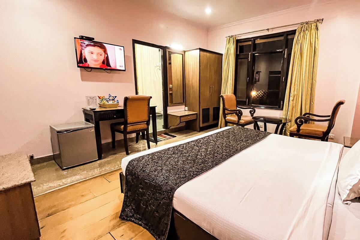 A hotel room with a bed, a desk, a chair, a television, and a wardrobe.