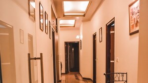 Un pasillo de hotel con piso alfombrado, cuadros en las paredes y una mesa con sillas.