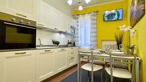 Une cuisine moderne avec des armoires blanches, un four encastré et un coin repas avec une table dressée pour quatre personnes.