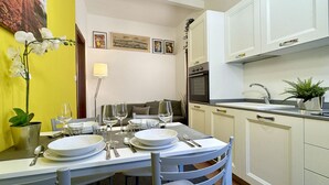 Un coin repas avec une table dressée pour quatre personnes, une cuisine équipée d’appareils modernes et un mur jaune agrémenté d’une plante orchidée.
