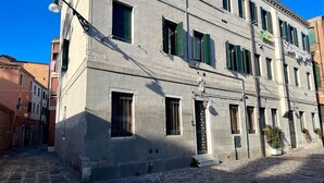 Un bâtiment historique doté de nombreuses fenêtres, dont certaines sont pourvues de volets, une façade en pierre et une rue étroite.