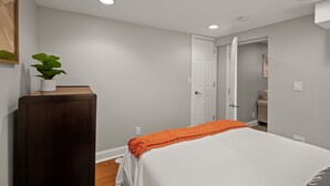 Un dormitorio con una cama, una mesita de noche, una planta en maceta y una puerta que da a otra habitación.