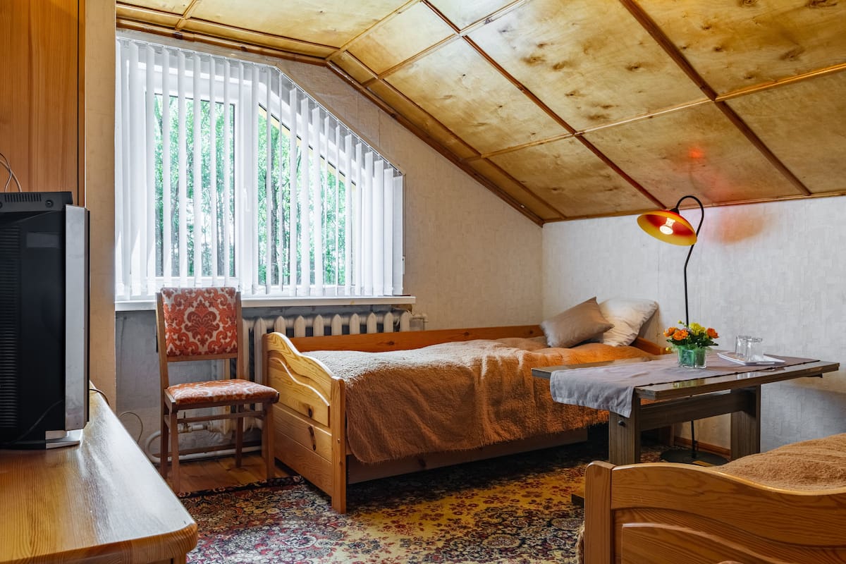 Una habitación acogedora con techo de madera, una cama, un escritorio, una silla y una ventana con persianas.