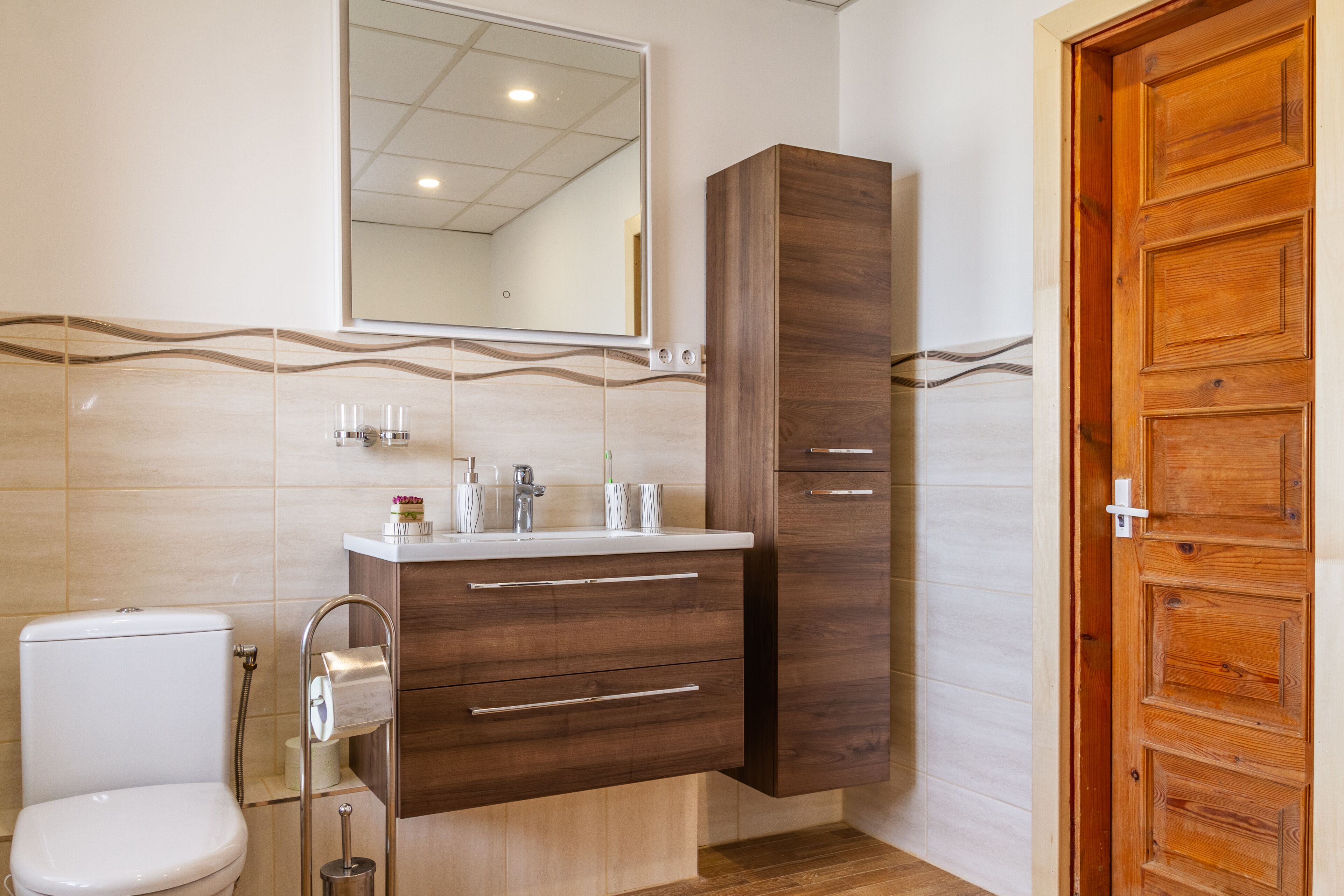 A bathroom with a toilet, a sink with a mirror above, wooden cabinets, and a wooden door.