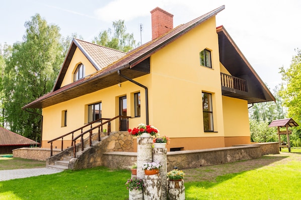 A two-story house with a stone staircase leading to the entrance, a balcony on the second floor, and a well-maintained lawn. - Guest house Sidrabi (Druva)