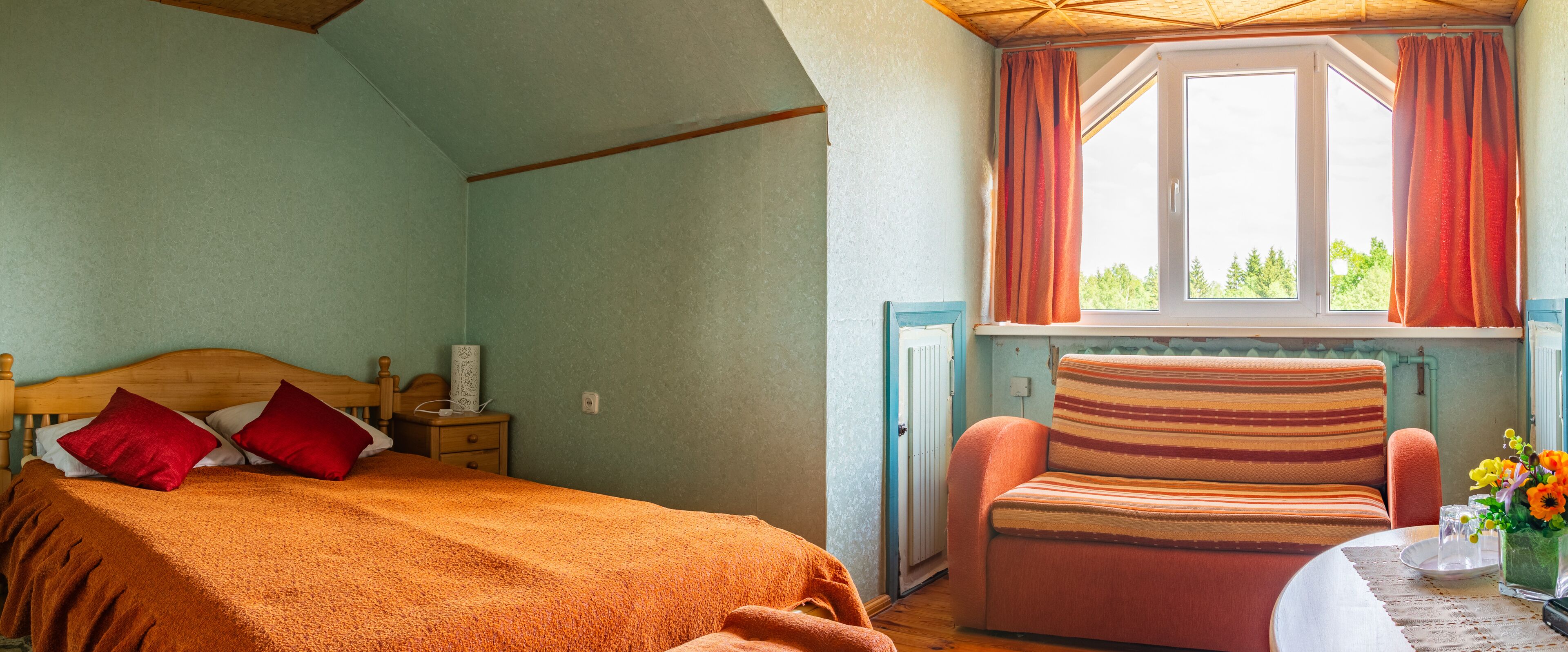 A bedroom with a bed, a chair, a window with curtains, and a radiator. - Guest house Sidrabi (Druva)