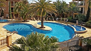 Una piscina de diseño curvo, rodeada de palmeras y sillas de descanso.