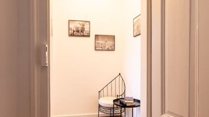 A hallway with a white door, a small black metal chair with a cushion, and two framed pictures on the wall. - Old Town Pearl: Two Bedromms - Wasching Machine - Parking (Pirna)