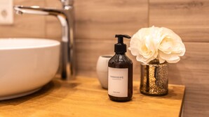 A bathroom with a white sink, a bottle of HANDSEIFE hand soap, and a vase with white flowers on a wooden countertop. - Old Town Pearl: Two Bedromms - Wasching Machine - Parking (Pirna)