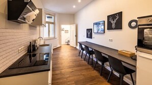 A modern kitchen with a black countertop, white cabinets, and a wooden floor. There are three black chairs at a long table, and a wall-mounted oven. - Old Town Pearl: Two Bedromms - Wasching Machine - Parking (Pirna)