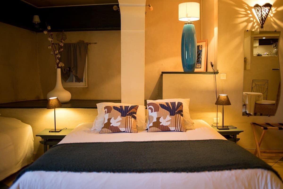 A hotel room with a bed, two bedside tables, a lamp, a vase with flowers, and a mirror.