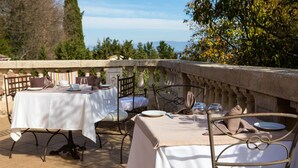An outdoor dining area with tables set for two, featuring white tablecloths and metal chairs. - In Provence Hôtel (Venelles)