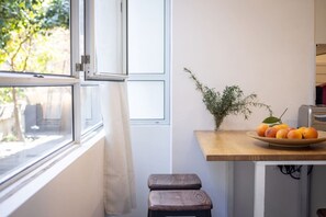 Et køkken med et vindue, en træskammel, en plante og en tallerken med frugt.