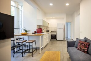 Eine moderne Küche mit weißen Schränken, einer zentralen Kochinsel mit Barhocker, einem grauen Sofa und einem Flachbildfernseher.