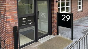 A modern building with a glass door entrance, a black awning, and a black sign with the number 29.