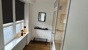 A narrow hallway with a radiator, a black mat, a shelf with decorative items, and a door with glass panels.