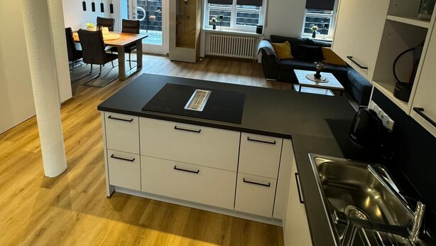 A modern kitchen with a central island, built-in appliances, and a dining area with a table and chairs.