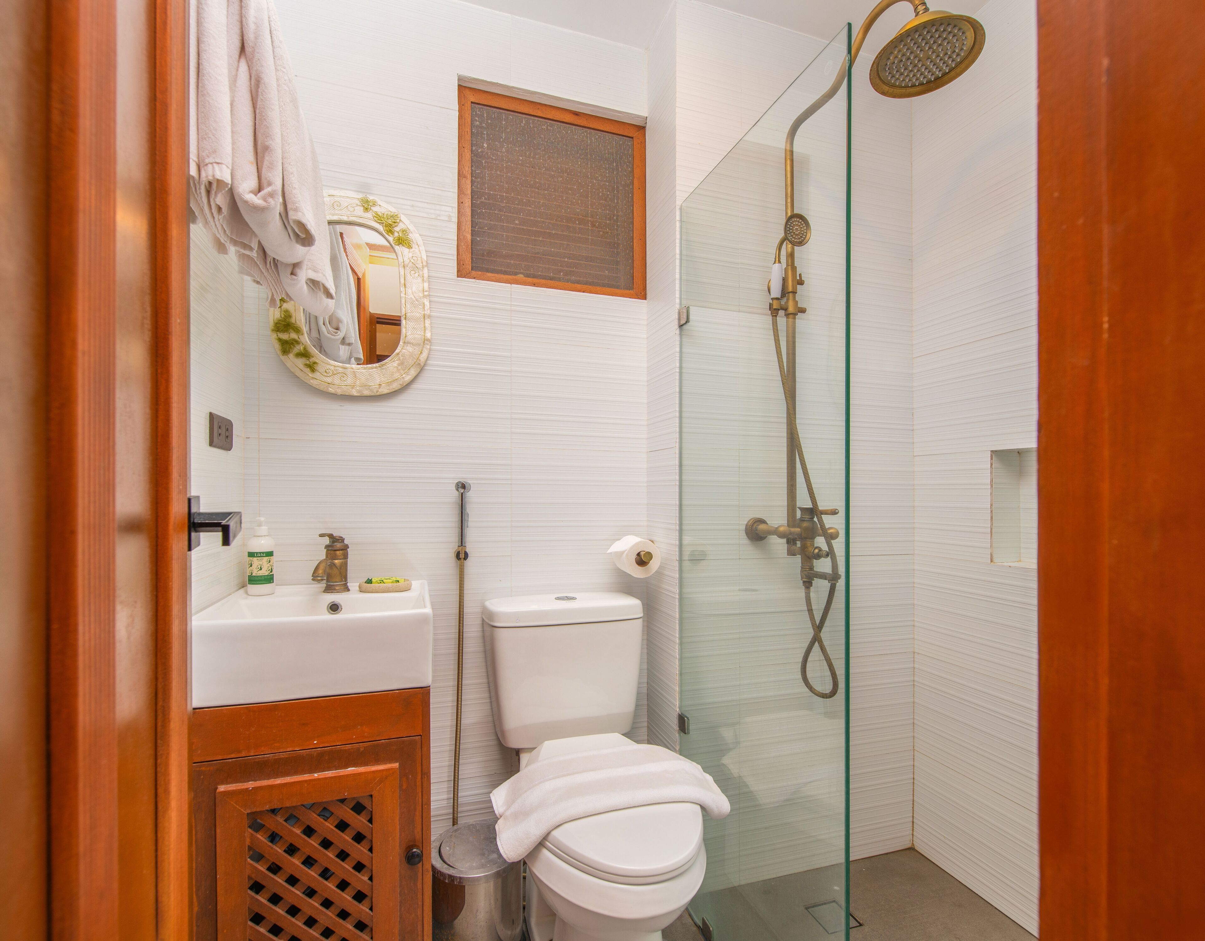 A bathroom with a toilet, sink, shower, and a wooden cabinet.