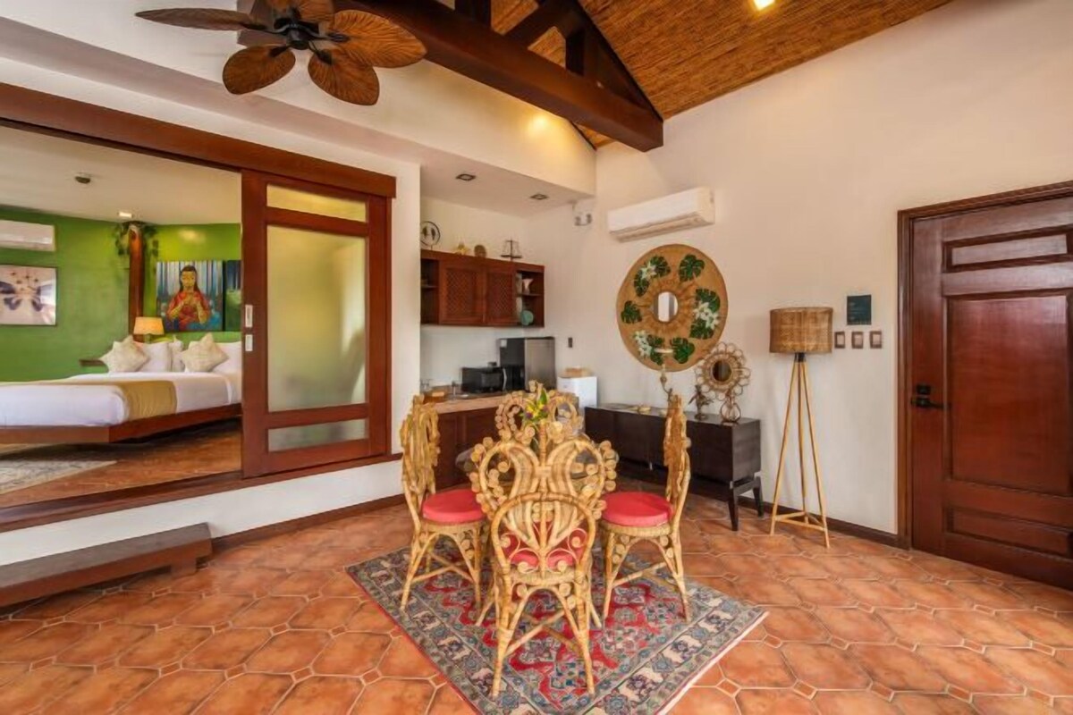 A room with a wooden ceiling, a dining table with ornate chairs, a patterned rug, and a large mirror on the wall.
