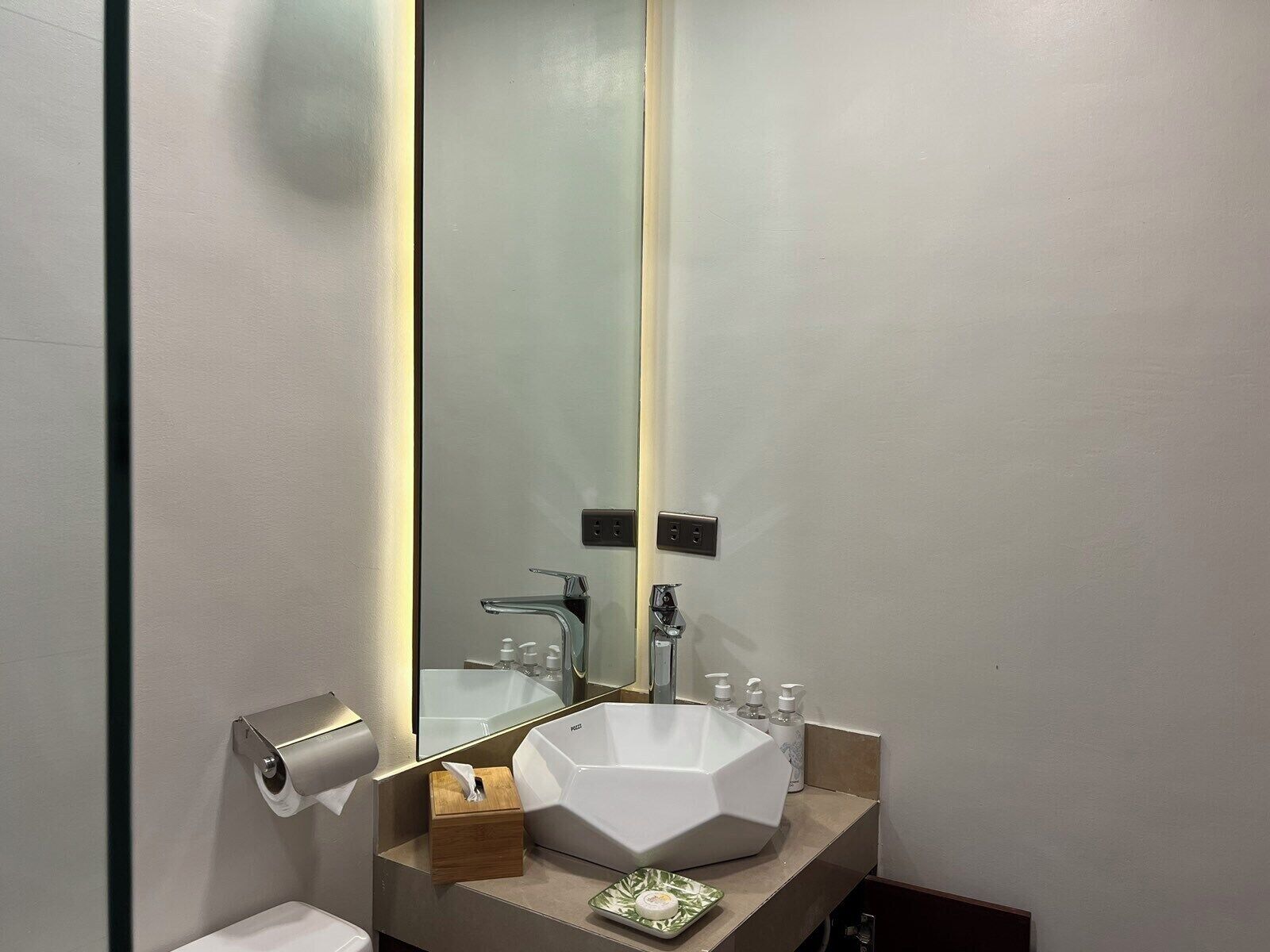 A modern bathroom with a large mirror, a white sink, and a toilet.