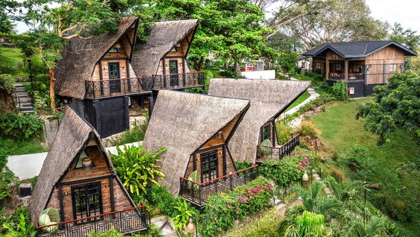 Une maison à toit de chaume, dotée d’un balcon et entourée d’une végétation luxuriante.
