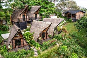 A thatched-roof house with a balcony, surrounded by lush greenery.